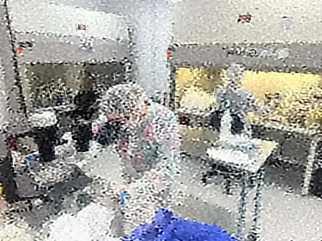 A lab technician in protective gear at a microscope